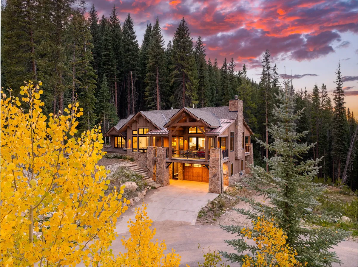 The chalet’s stone facade is framed by vibrant yellow foliage, with expansive windows hinting at the cozy interior. The evening sky above adds dramatic flair, while the setting suggests ample space for outdoor gatherings, nature walks, and wildlife encounters.
