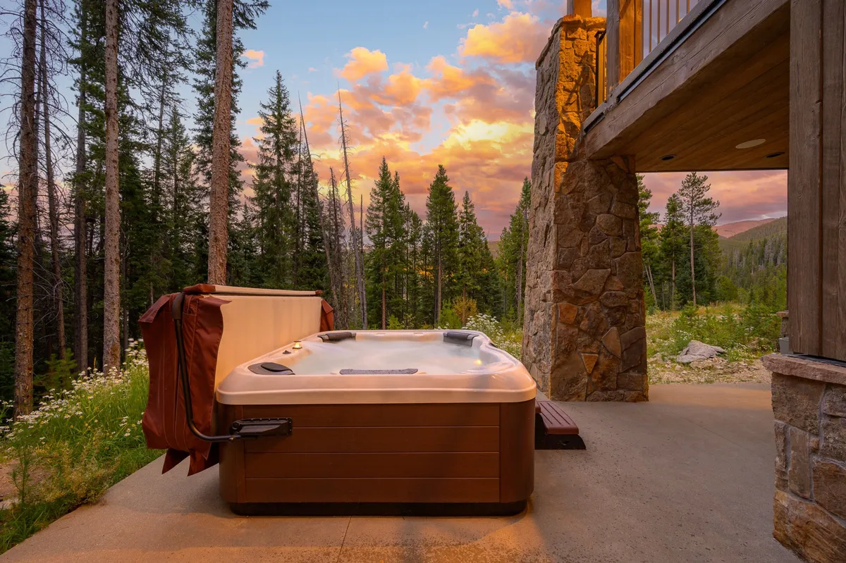 This image captures a secluded hot tub surrounded by towering pines and set against a stunning sunset sky, with guests relaxing in the warm water. The serene natural setting highlights the forest backdrop and tranquil atmosphere, ideal for unwinding after outdoor adventures.
