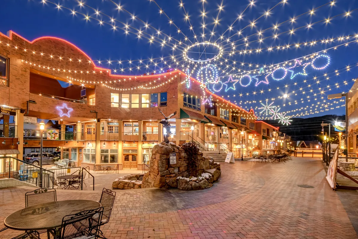 A lively downtown scene featuring string lights, decorated buildings, and a stone fountain. Guests stroll, dine outdoors, and shop, highlighting the vibrancy of the local area—even in the off-season.