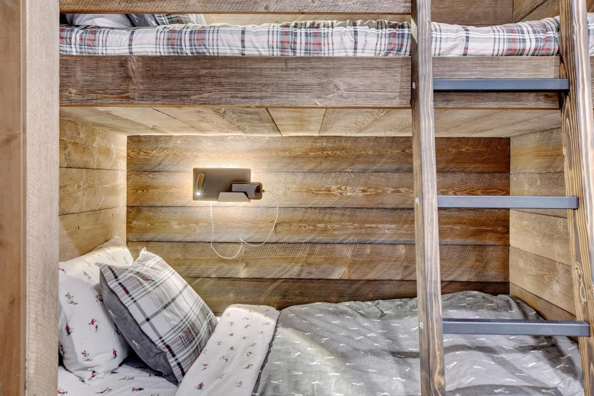 A cozy bunk room with built-in bunk beds adorned with plaid bedding and warm wooden wall accents. The space feels playful yet inviting, perfect for children to enjoy memorable sleepovers, bedtime stories, or quiet reading.