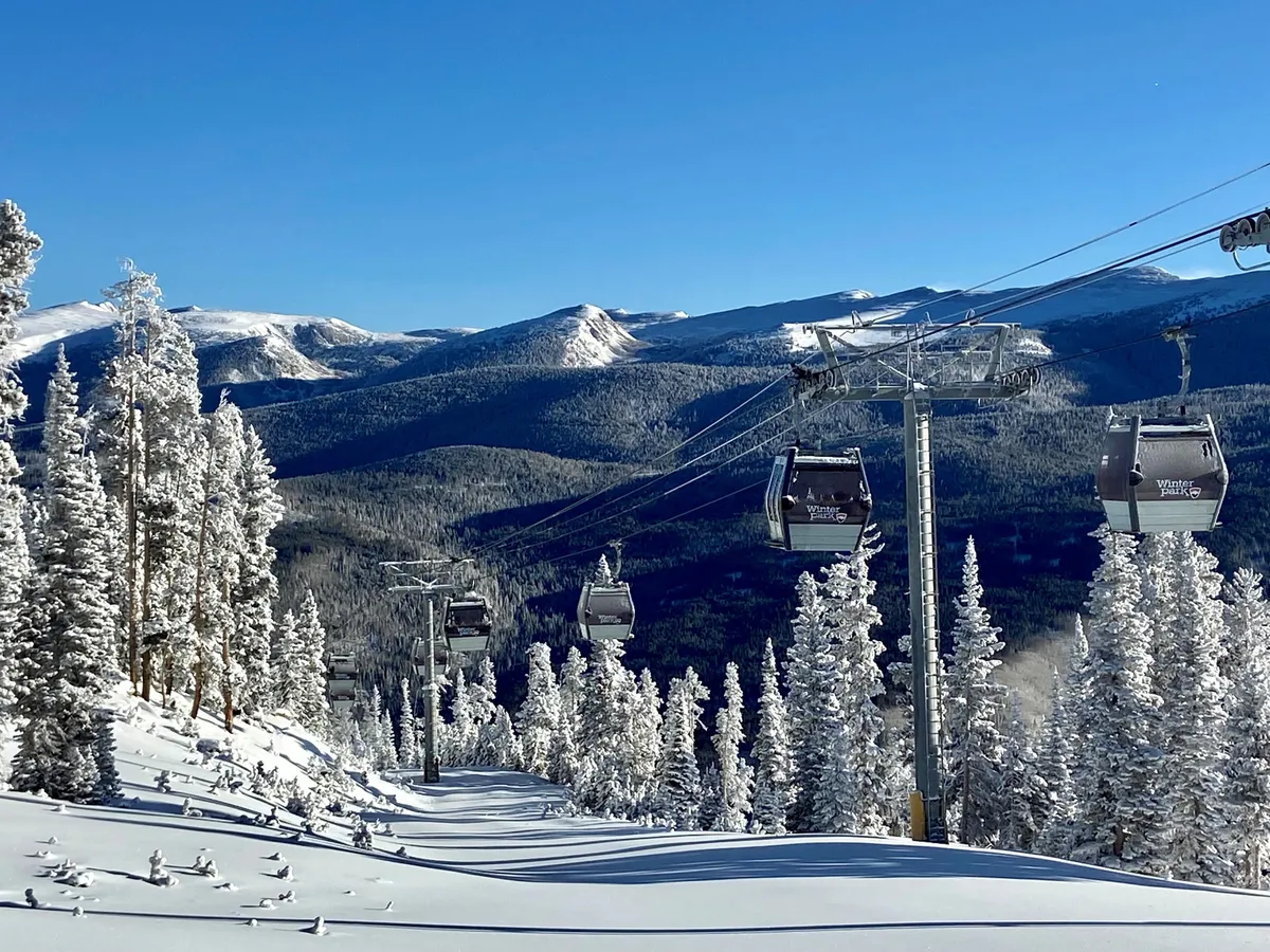A breathtaking winter landscape with ski lift gondolas ascending snow-covered mountains, flanked by frosted trees and wide, open slopes. The scene is serene yet adventurous, inviting guests to explore the Rockies in wintertime.