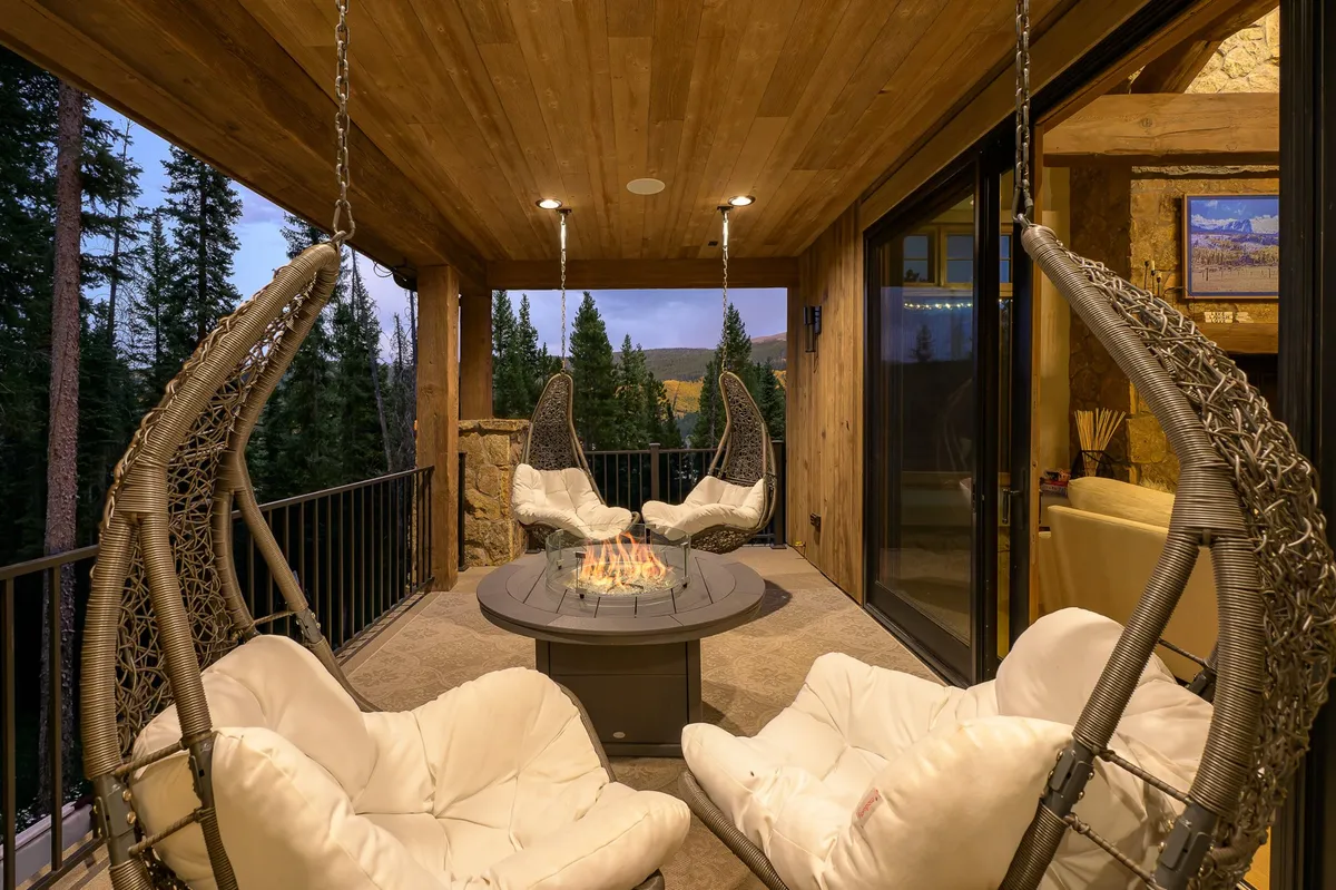 The scene features a cozy outdoor seating area with hanging chairs positioned around a glowing gas fire pit, all set with a view of the forest. The atmosphere is tranquil and intimate, inviting guests to gather for s'mores, storytelling, or stargazing in a secluded setting.