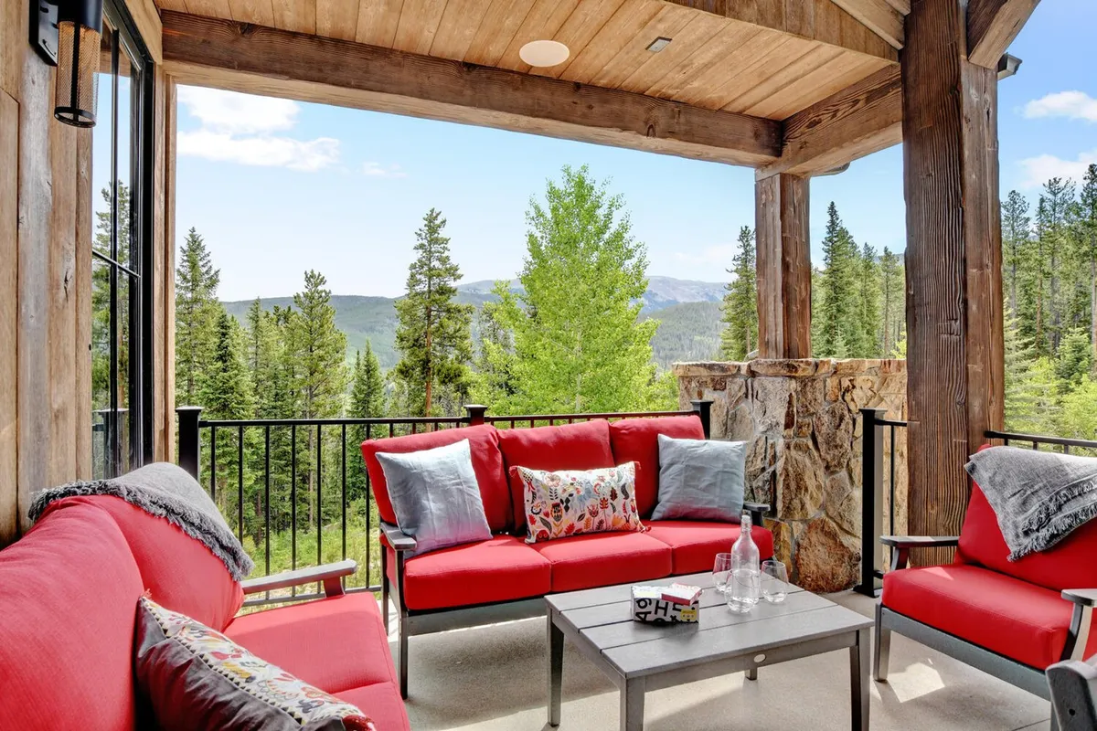 An inviting outdoor living space features red seating and a coffee table positioned to enjoy sweeping mountain and tree views. The setting is ideal for socializing, relaxing, and connecting with nature.