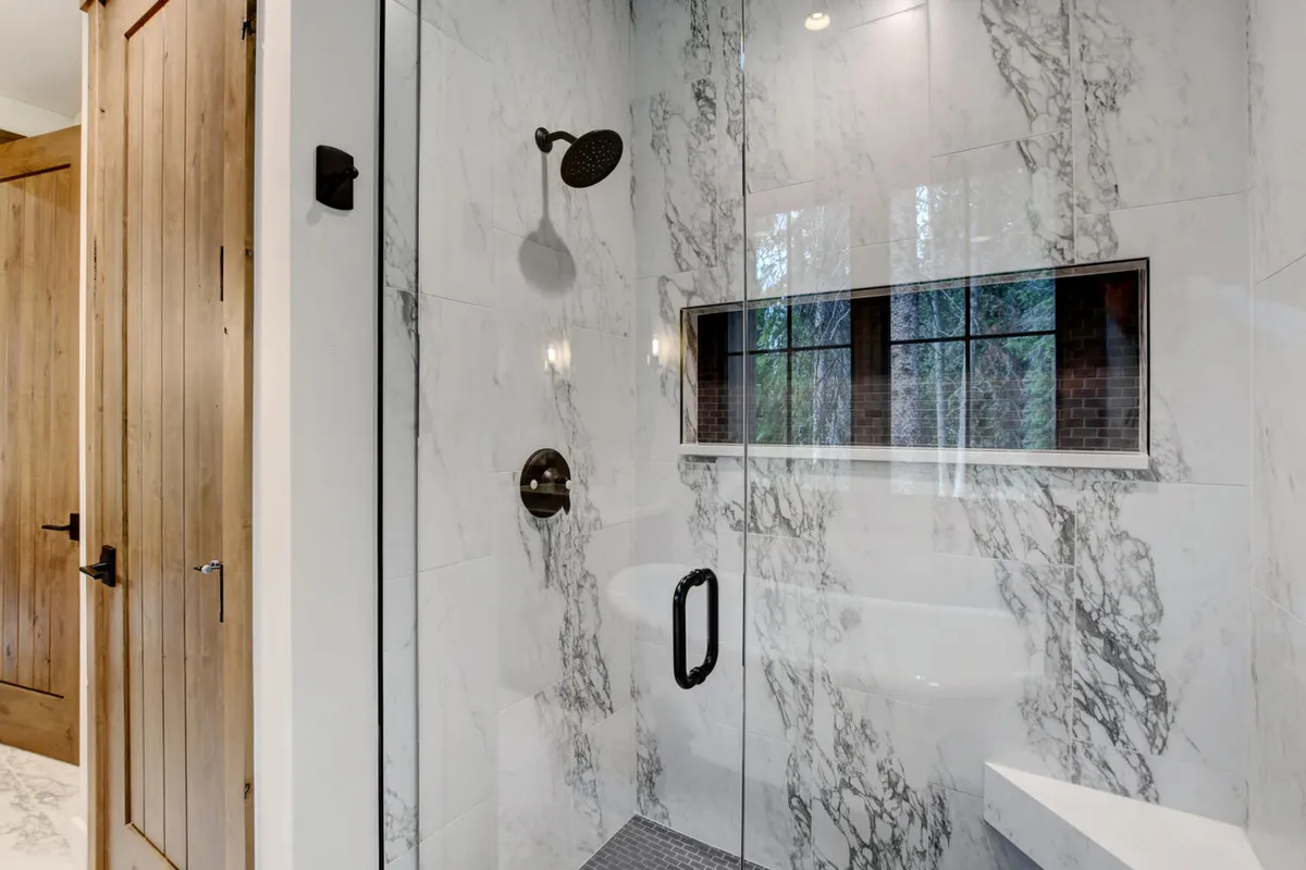 A luxurious bathroom highlighted by a glass shower enclosure, elegant marble walls, and a window that lets in natural light. The space exudes a spa-like tranquility, encouraging relaxation and self-care routines.