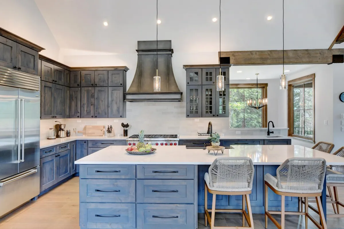 A modern chef’s kitchen with a large island, stainless steel appliances, hanging light fixtures, and exposed wooden beams. The open layout is designed for group cooking, informal meetings, and celebratory meals.