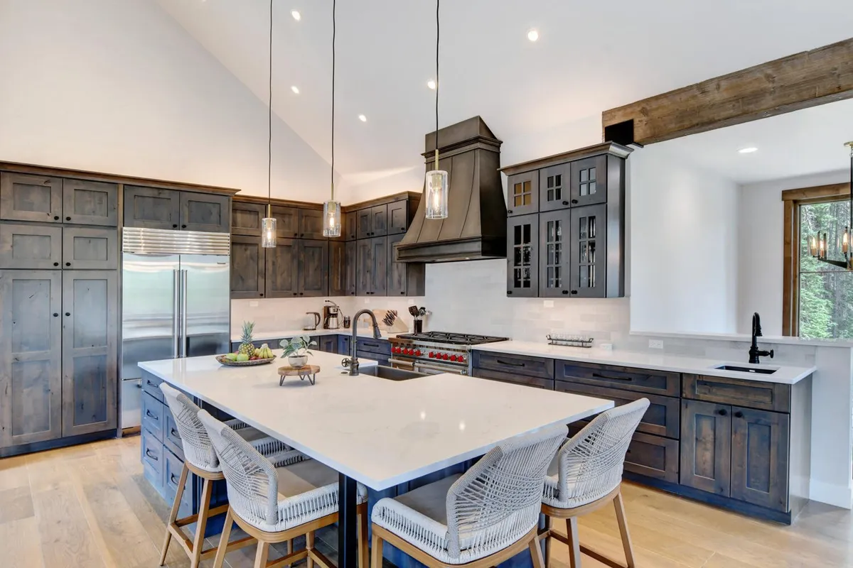 A modern kitchen centered around a large granite island with seating, flanked by professional stainless steel appliances and dark wood cabinetry. Pendant lights cast a welcoming glow, and the open design facilitates both culinary creativity and social interaction.