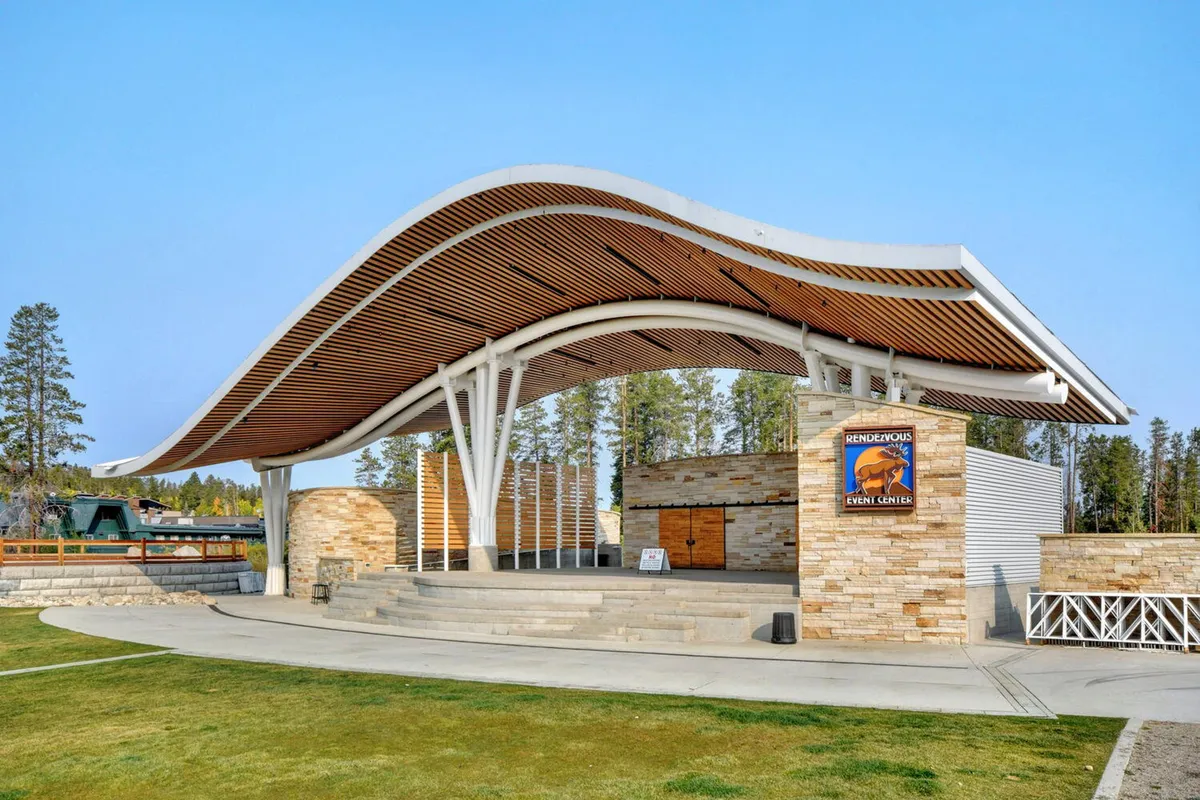 This image captures the distinctive curved roof structure and stone wall of the Hideaway Park Amphitheater's stage area, set outdoors. The scene is designed for gatherings, concerts, and community events, conveying a sense of vibrant, communal entertainment that ties into the nearby attractions mentioned in the section.